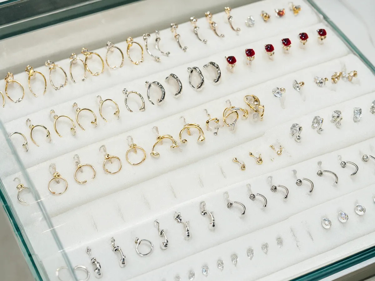 Gold and titanium hoops, barbells and red and green gemstone studs in a glass display case